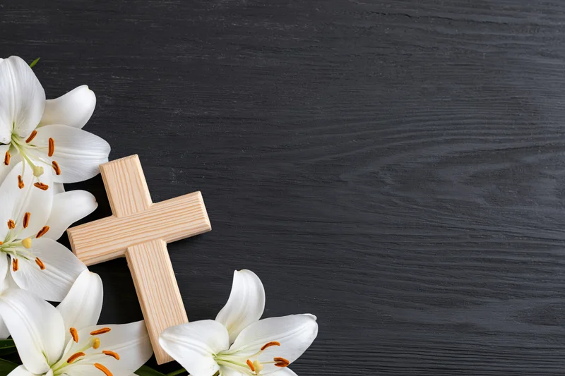 Wooden cross and white lilies arranged on dark wood surface with copyspace