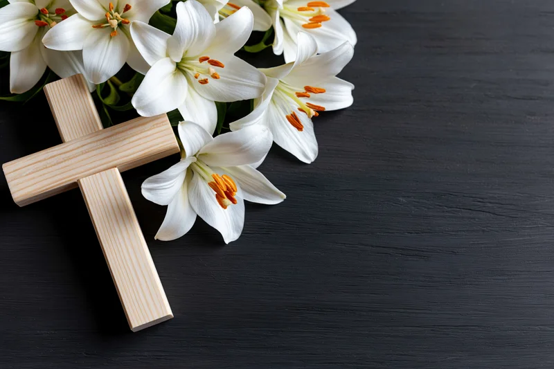 Wooden cross with white lilies arranged on dark surface