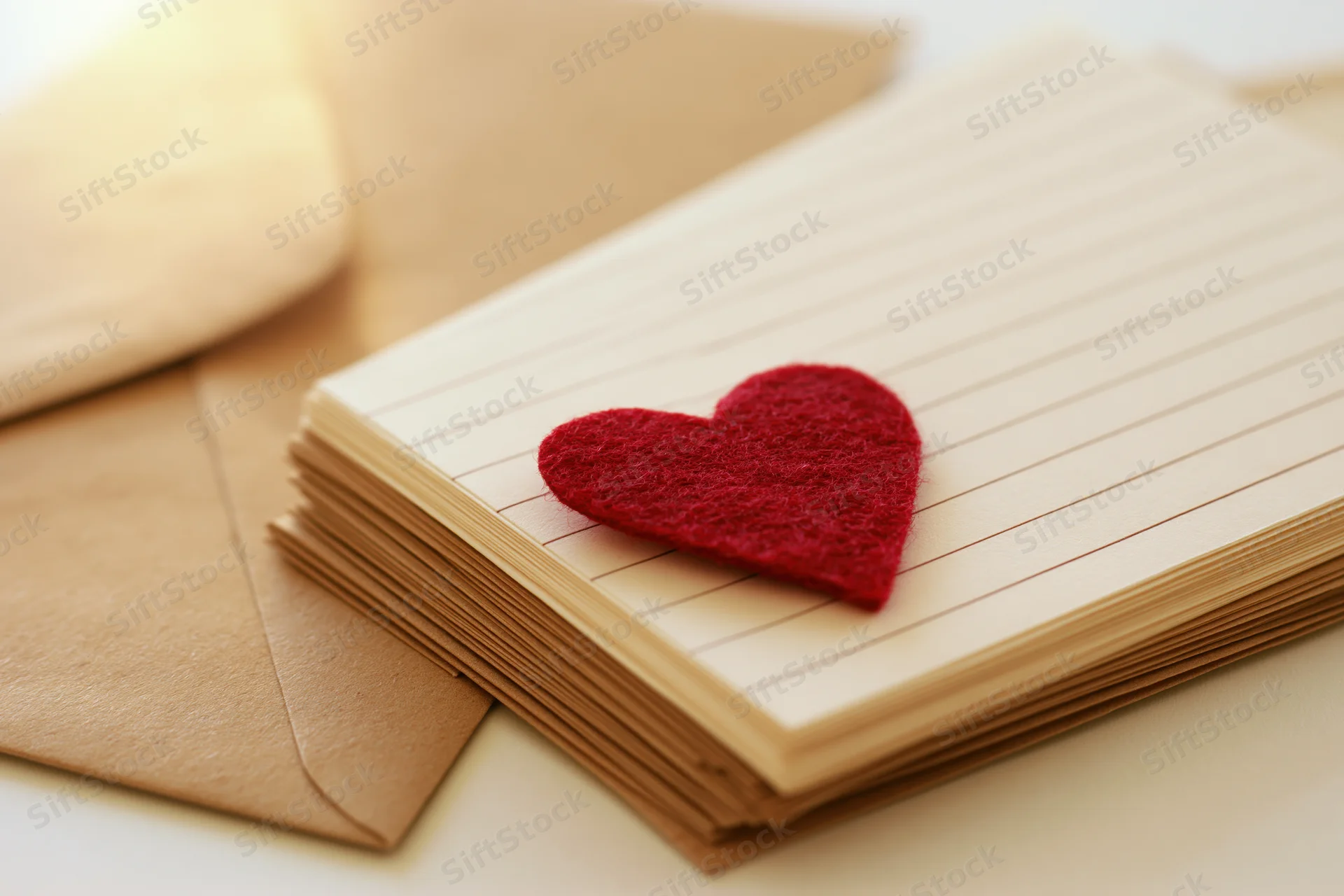 Red felt heart on stack of lined notebook paper beside kraft envelope