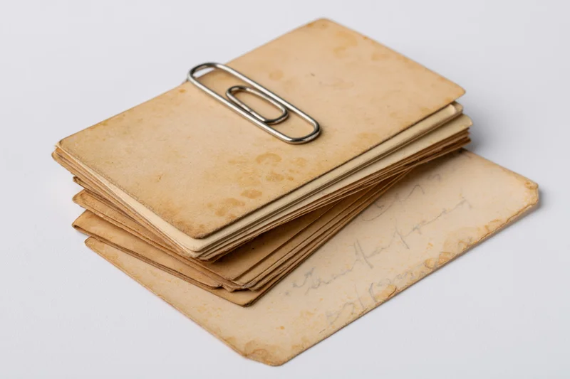 Stack of aged yellowed paper cards and postcards held together by a metal paperclip on white background
