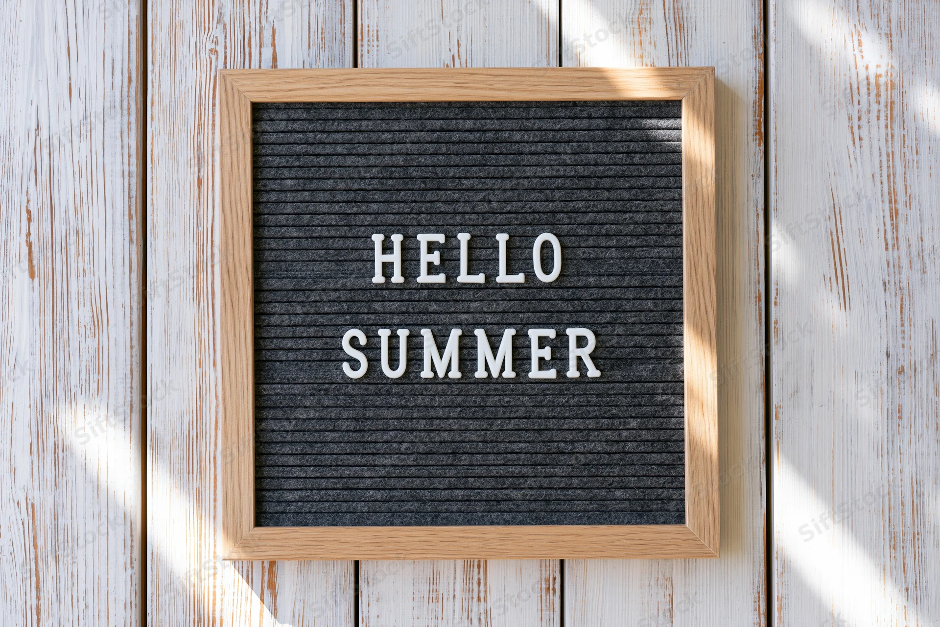 Square felt letterboard with hello summer text mounted on whitewashed wood wall