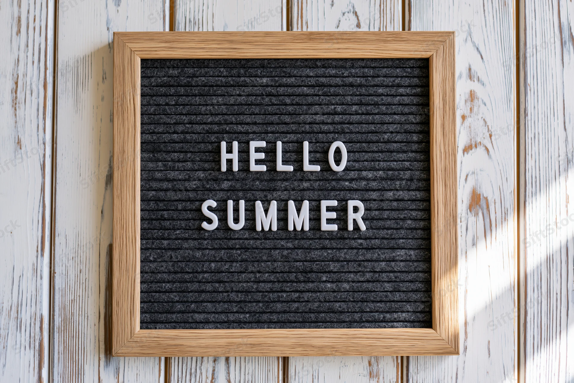 Letterboard with hello summer text mounted on whitewashed wood wall