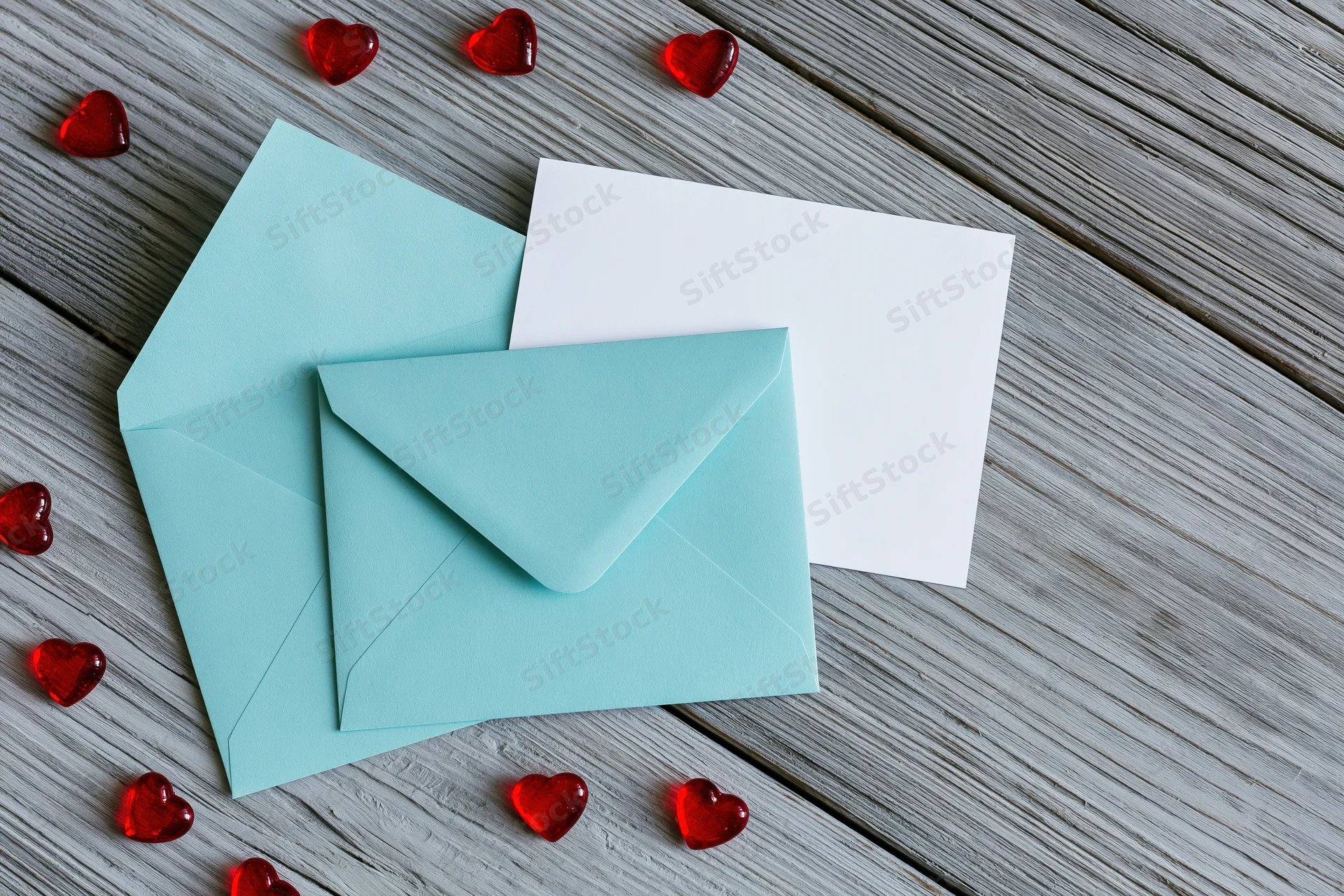 Teal mint envelope and blank white card on weathered wooden surface with red heart decorations