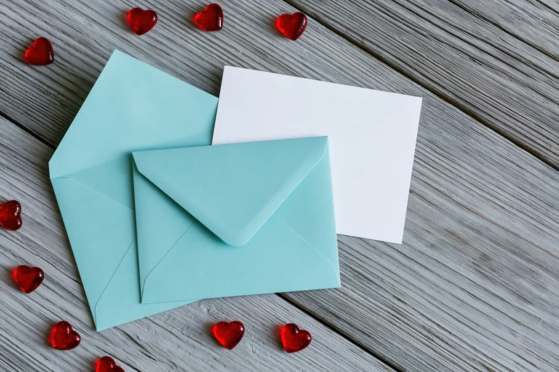 Teal mint envelope and blank white card on weathered wooden surface with red heart decorations