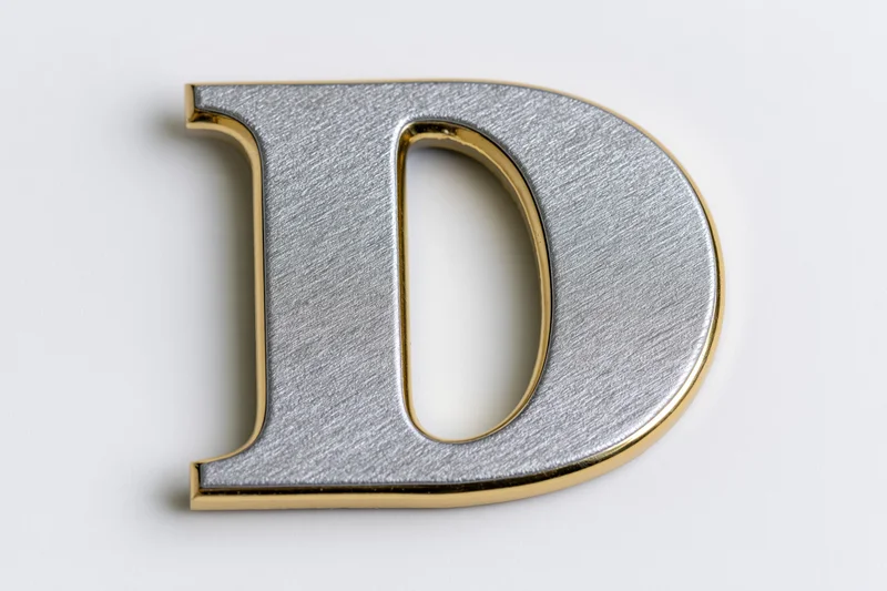 Three-dimensional uppercase letter d with matte silver face and gold trim on white background