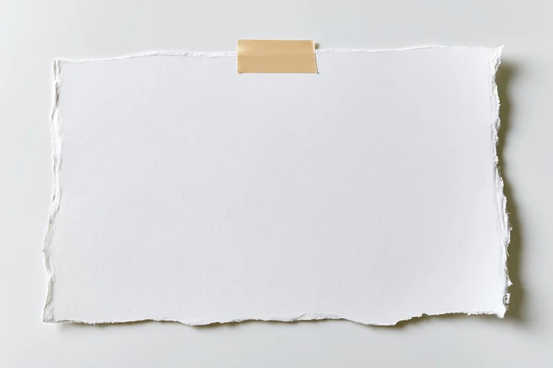 Torn white paper sheet taped to a plain surface with beige adhesive strip, flat lay view