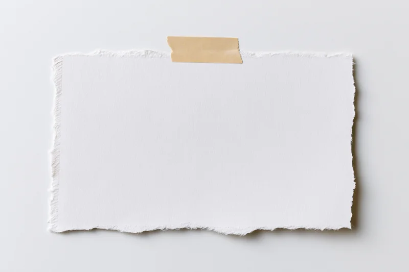 Torn white paper sheet taped to a plain surface with beige adhesive strip