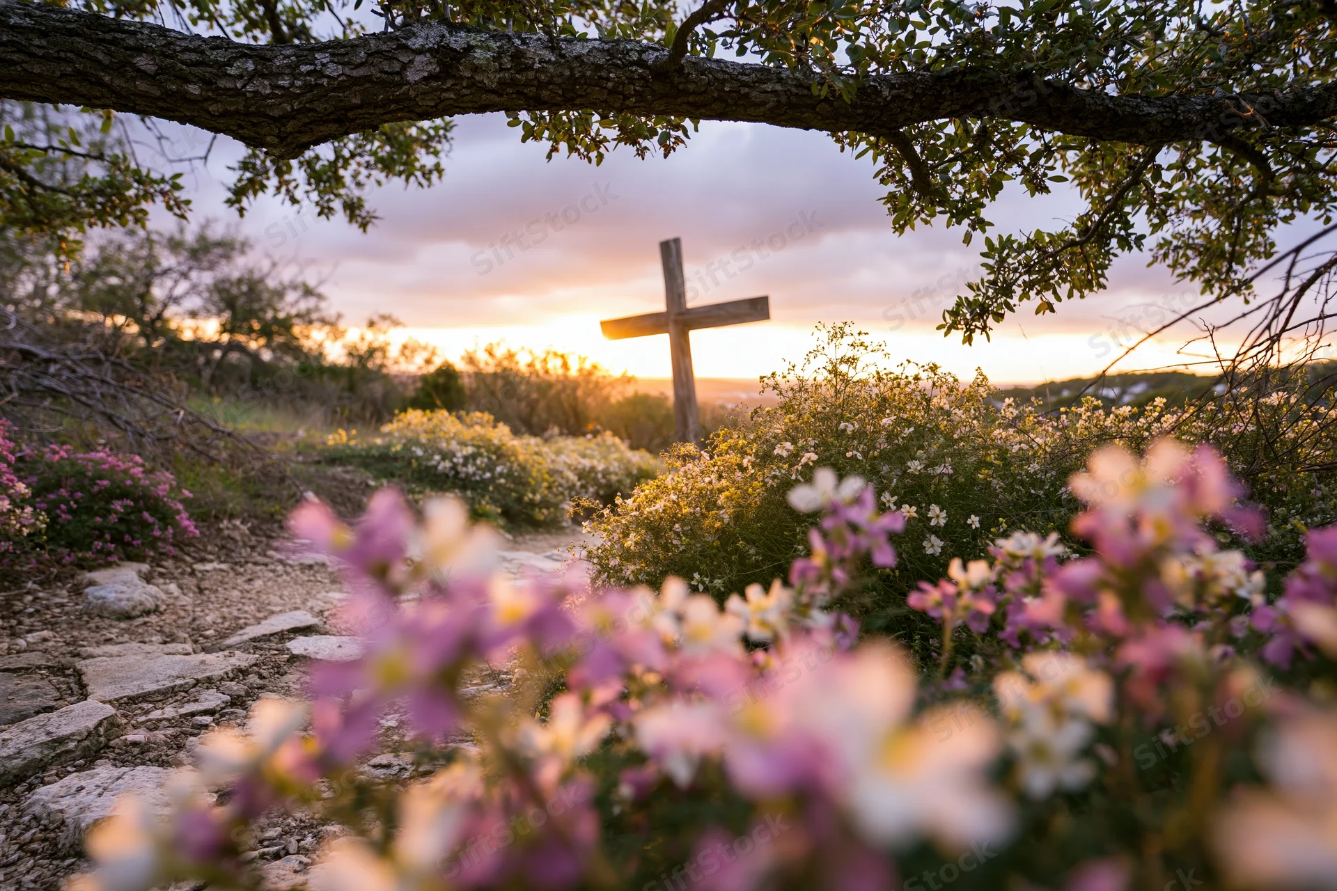 Wooden cross on a hillside path at sunset surrounded by wildflowers and stone steps