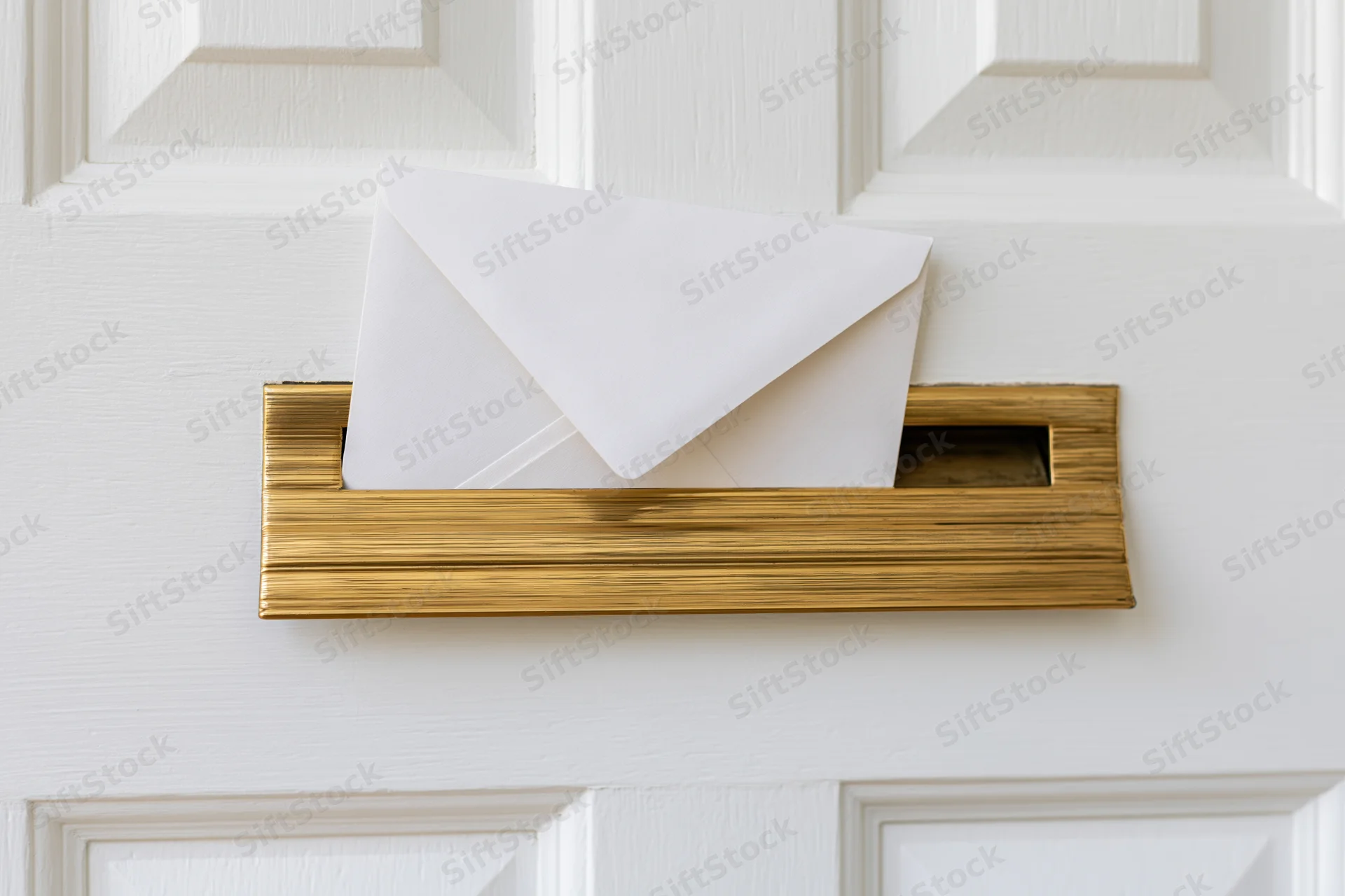 White envelope partially inserted into brass mailbox on white door