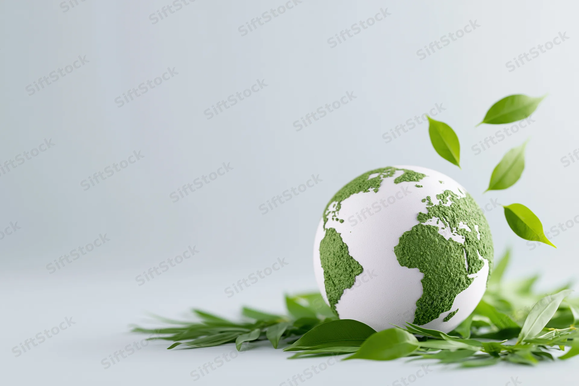 White globe with green textured continents surrounded by floating leaves on a light surface