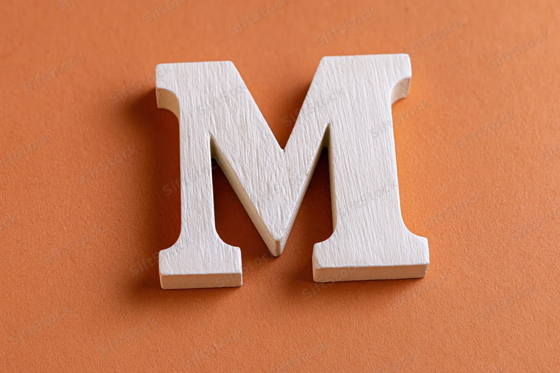 White wooden letter m resting flat on textured orange surface