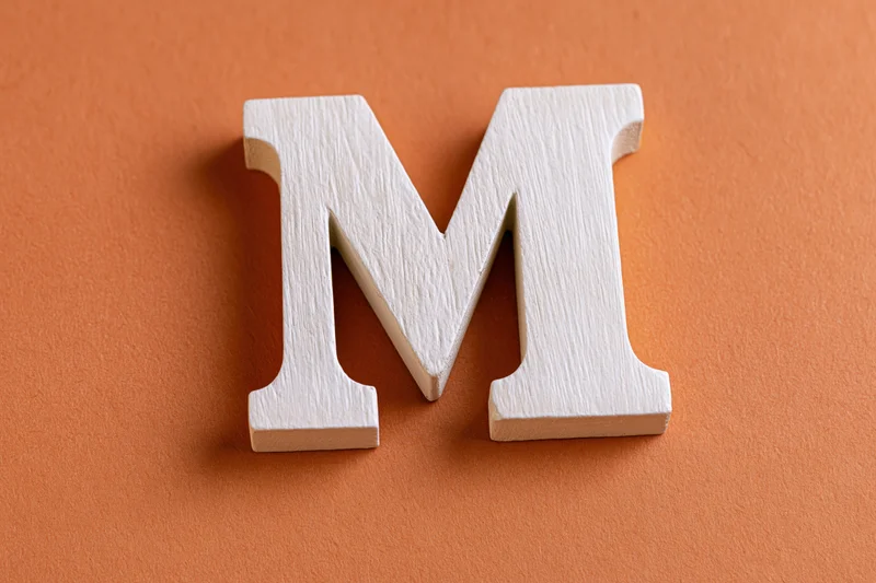 White wooden letter m resting flat on textured orange surface