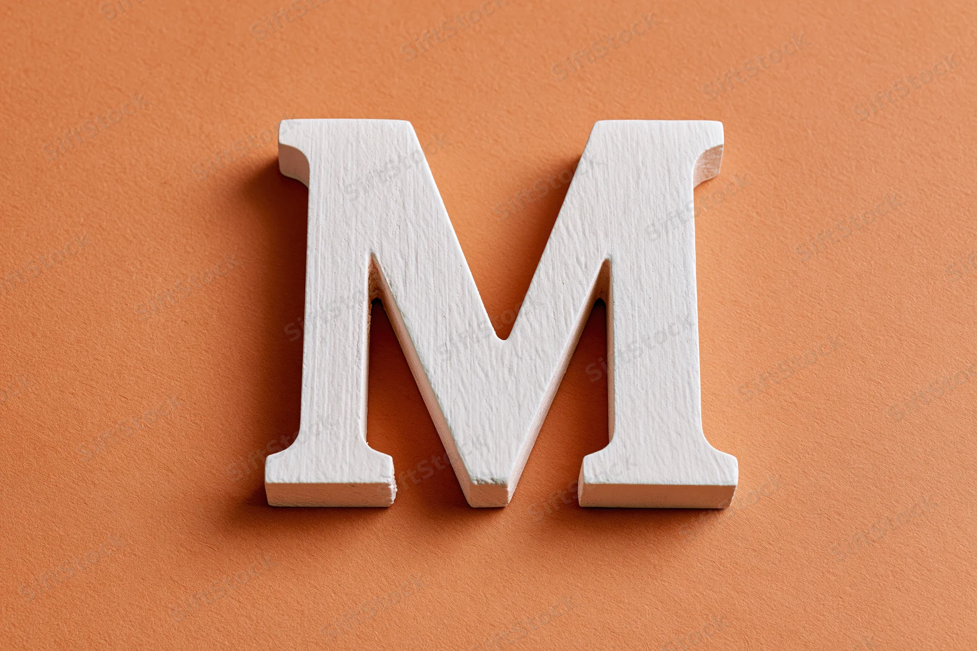 White wooden letter m resting flat on textured orange surface