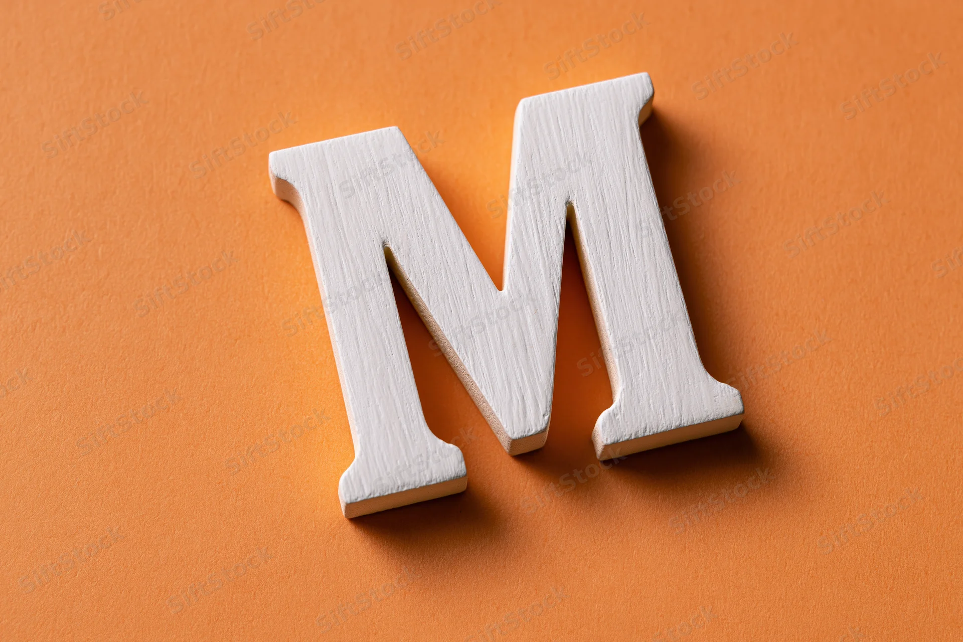 White wooden letter m resting on textured orange surface