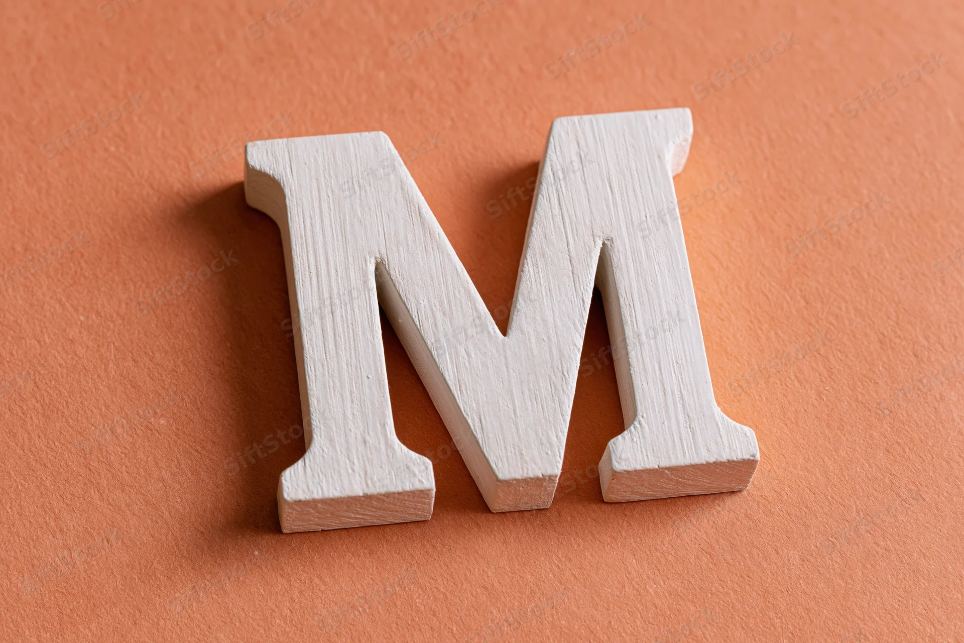 White wooden letter m resting flat on textured orange surface