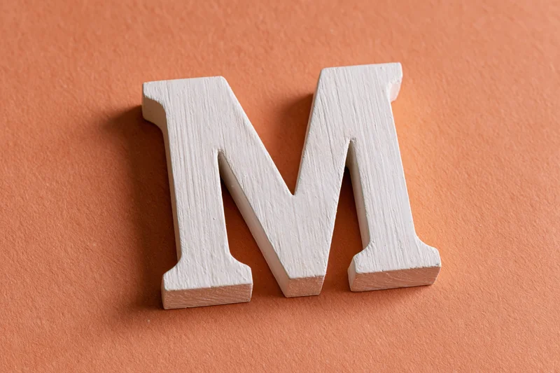 White wooden letter m resting flat on textured orange surface