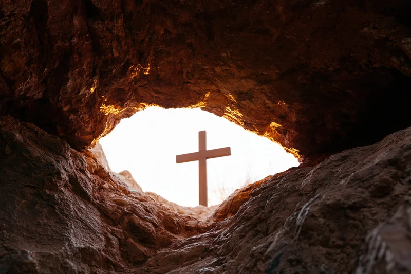 Wooden christian cross silhouetted at cave entrance against bright sky