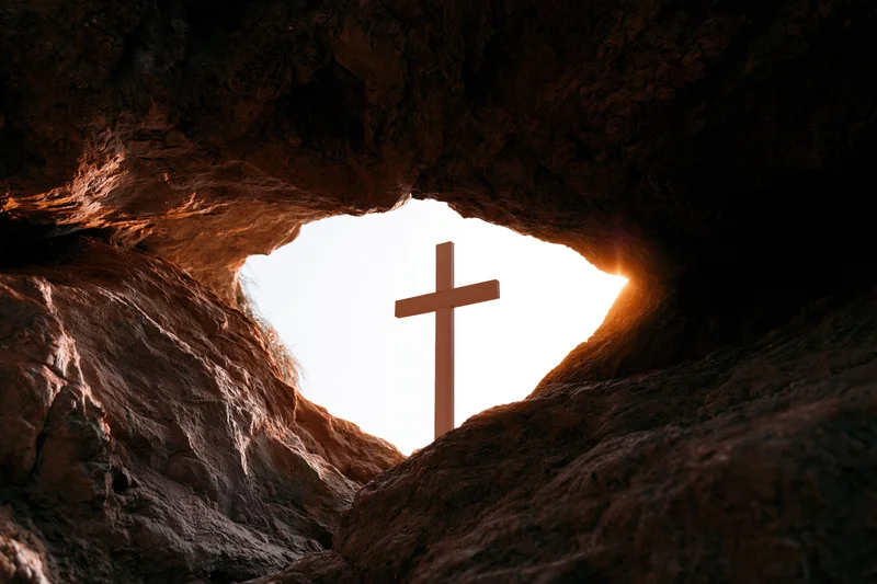 Wooden christian cross silhouetted at cave entrance against bright sky