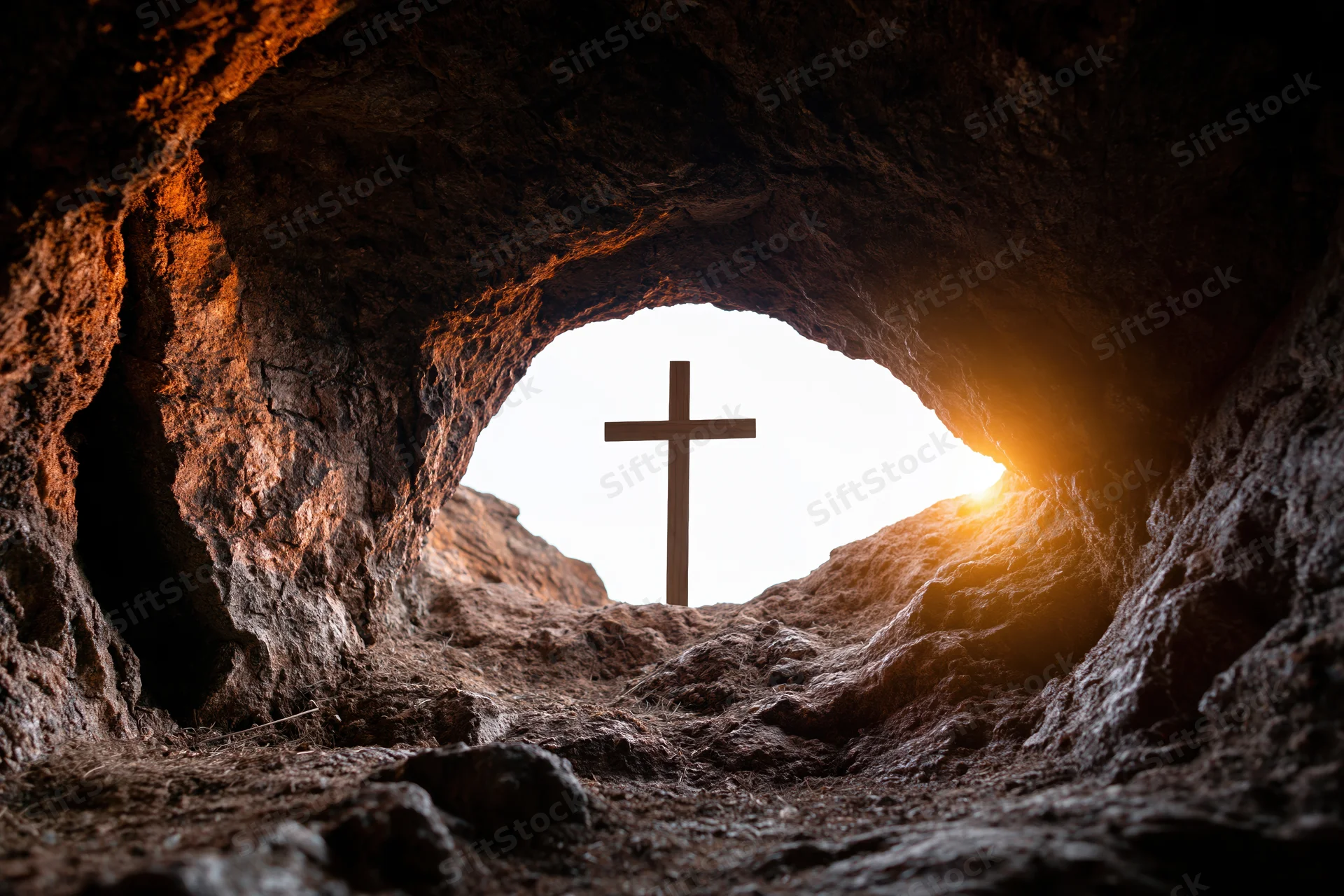 Wooden cross silhouetted at cave entrance with sunlight streaming through rocky opening