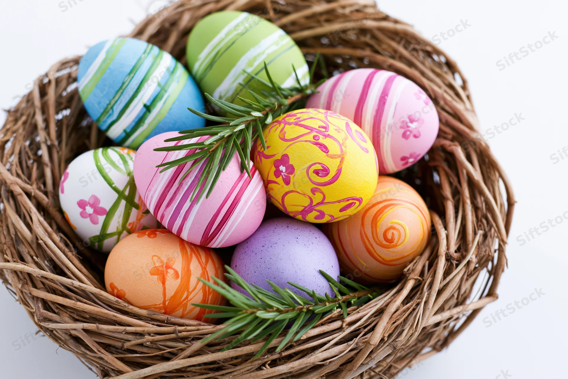 Hand-painted easter eggs in a woven twig nest with pine sprigs on white background