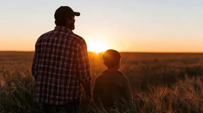 Father and son standing side by side in a wheatfield at sunset