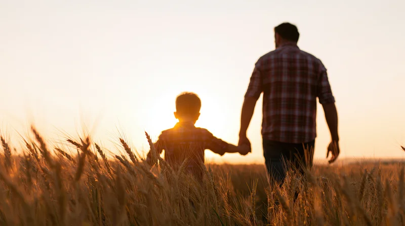 Father and son walking hand in hand through a wheat field at sunset