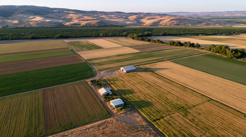 Aerial view of patchwork farmland with cultivated fields and small farm buildings in rural countryside