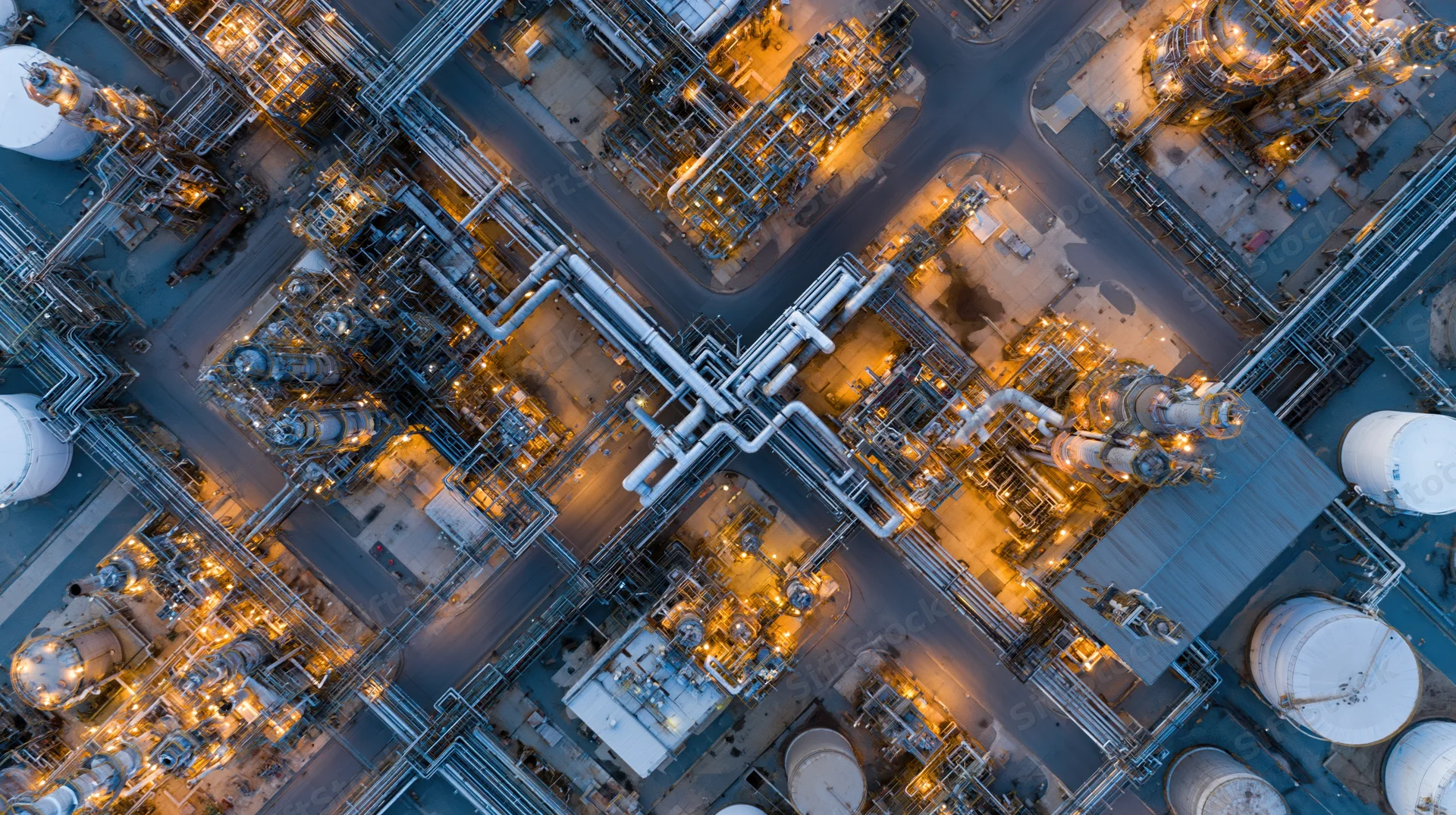 Aerial top-down view of a large oil refinery and petrochemical plant at night with illuminated pipelines and storage tanks