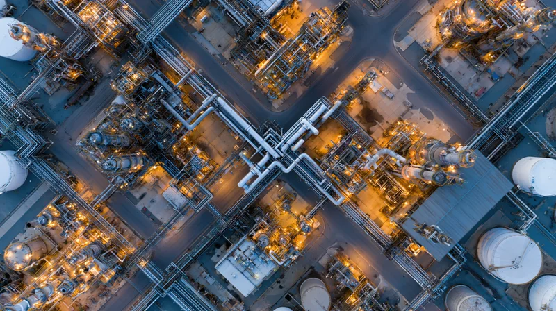 Aerial top-down view of a large oil refinery and petrochemical plant at night with illuminated pipelines and storage tanks