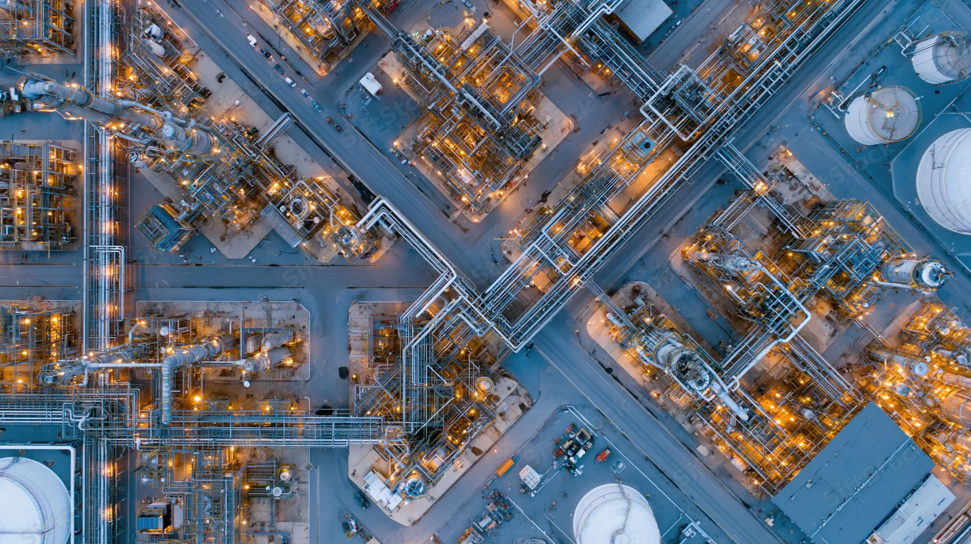 Aerial top-down view of a large oil refinery and petrochemical plant at night with illuminated structures and pipelines