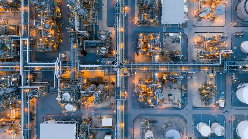 Aerial top-down view of a large oil refinery and petrochemical plant at night with illuminated pipelines and storage tanks