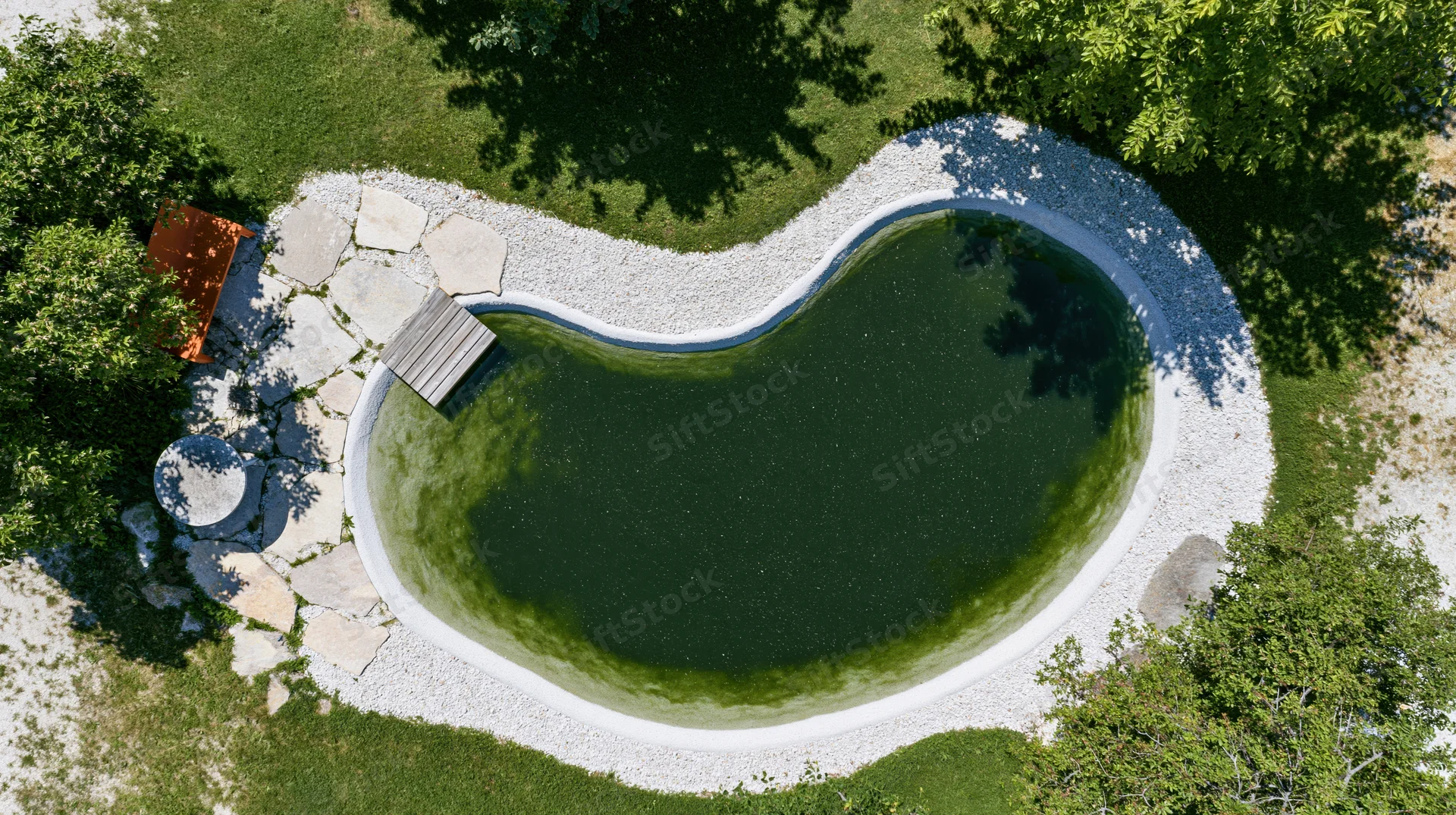 Aerial top-down view of a natural swimming pond surrounded by grass, trees, and stone pathways in a garden setting