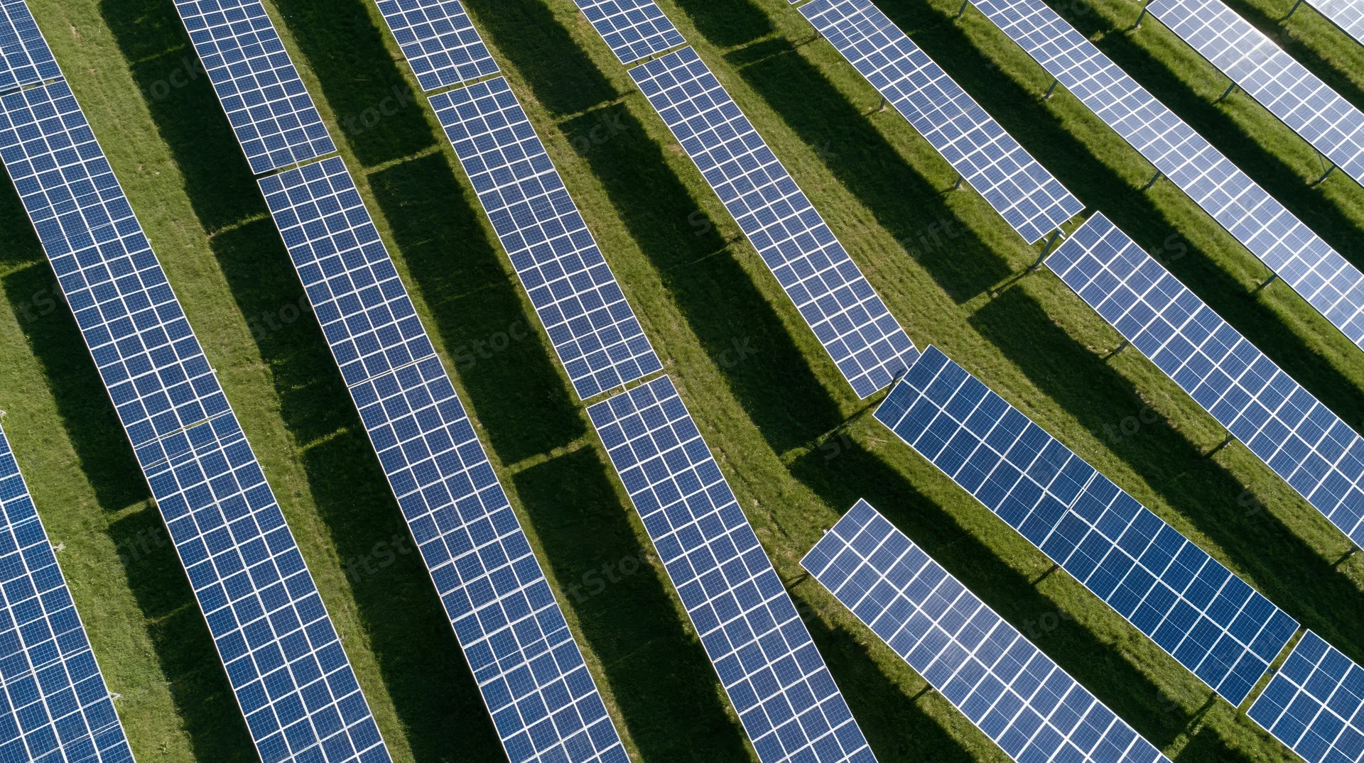 Aerial view of rows of photovoltaic panels in a grassy field