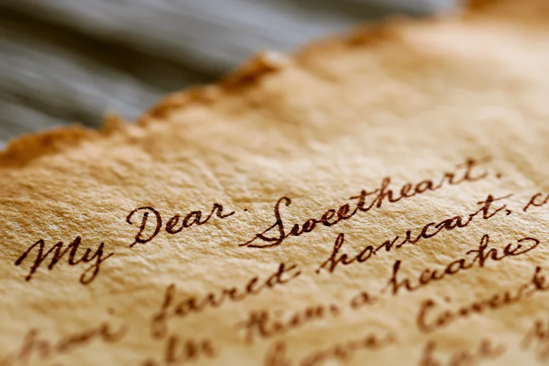 Close-up of aged handwritten love letter on yellowed parchment paper with cursive script reading "My Dear Sweetheart