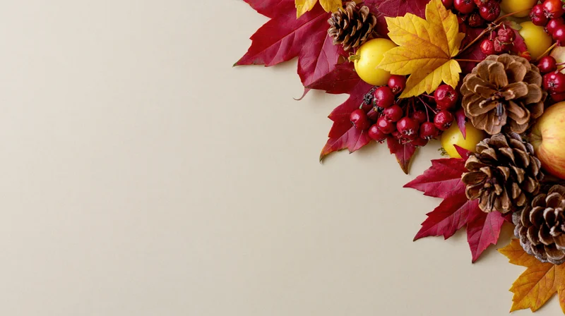 Autumn flat lay with red and yellow maple leaves, pinecones, berries, and apples arranged in corner on beige surface