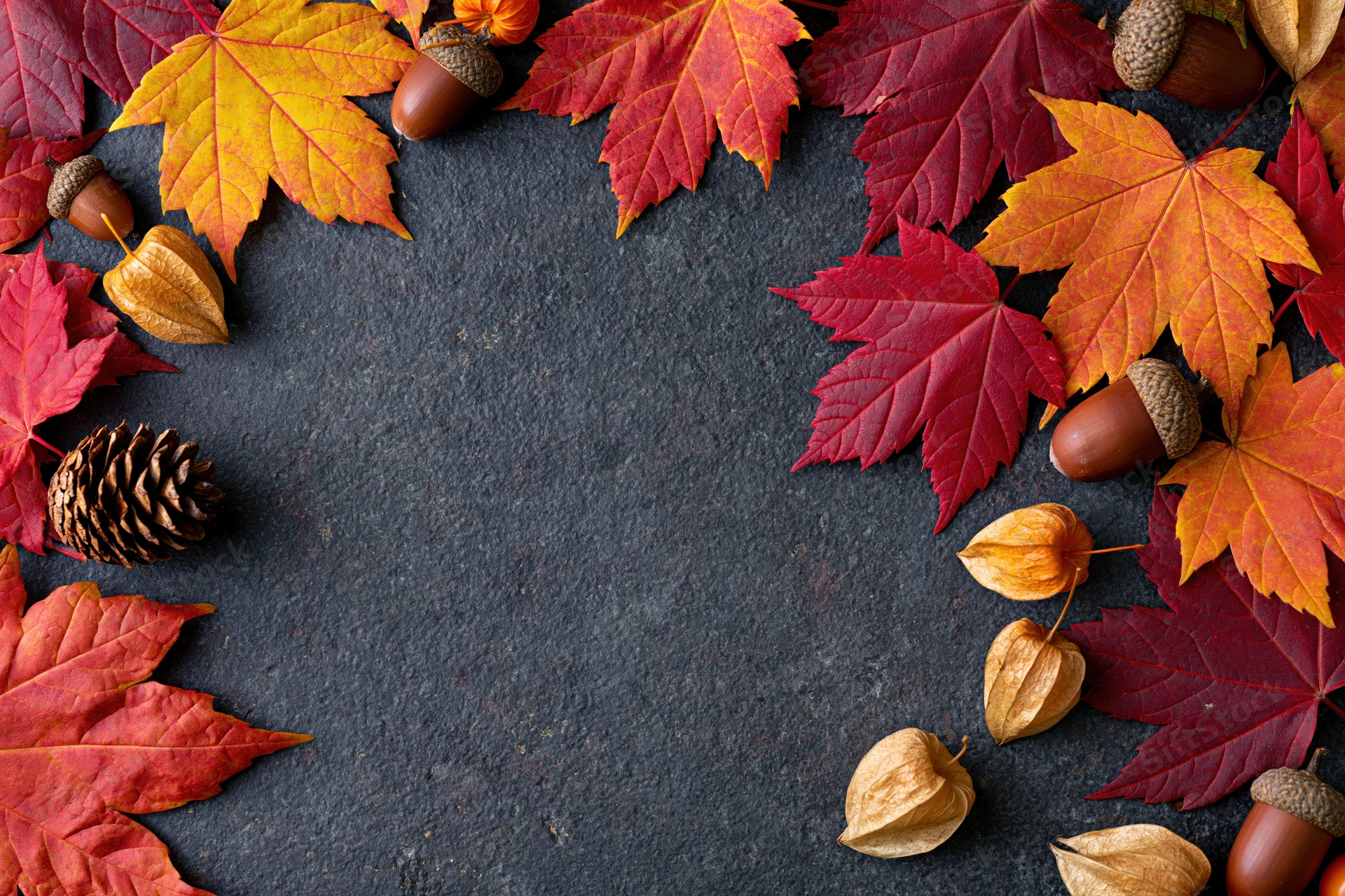 Autumn maple leaves and acorns arranged in a border on dark stone surface with copyspace