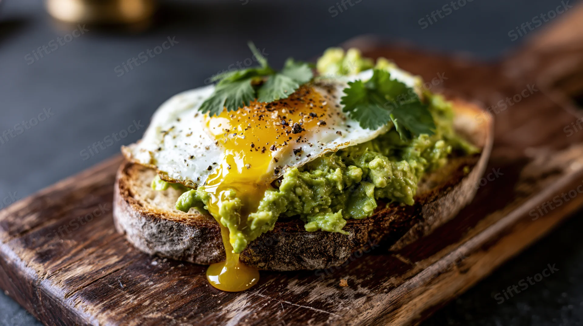Avocado toast with runny fried egg and cilantro on thick sourdough bread on wooden cutting board
