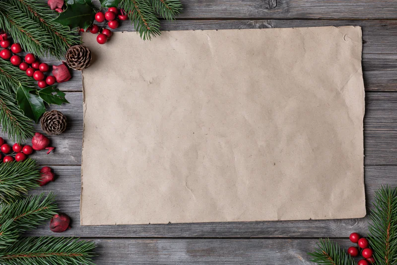 Blank aged kraft paper sheet on weathered wooden surface surrounded by christmas decorations