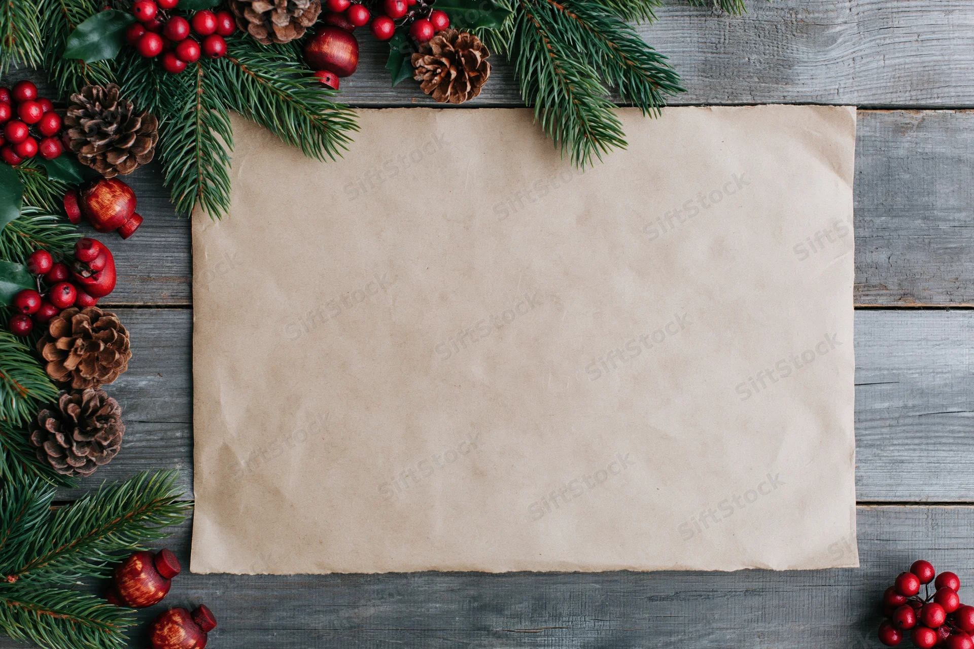 Blank aged kraft paper sheet on weathered grey wood surrounded by christmas decorations