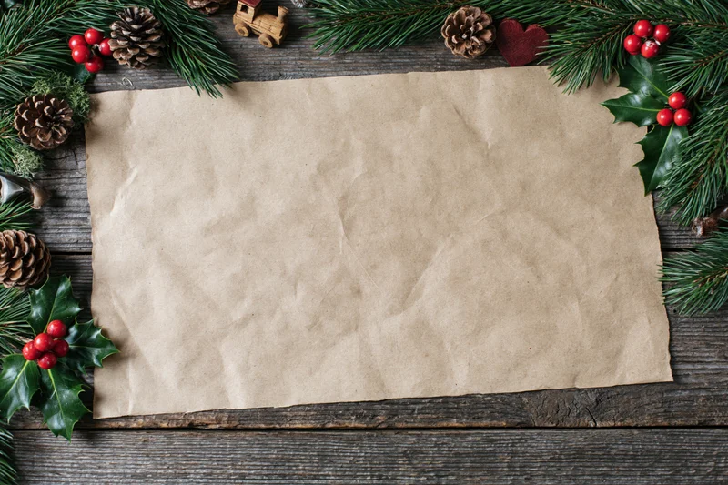Blank kraft paper sheet on weathered wooden surface surrounded by christmas decorations