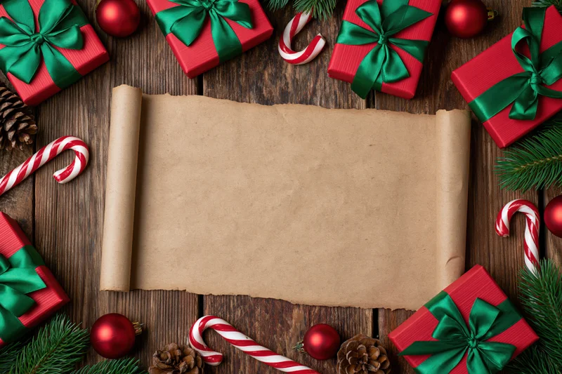 Blank parchment scroll on wooden table surrounded by red gifts, candy canes, pinecones and ornaments