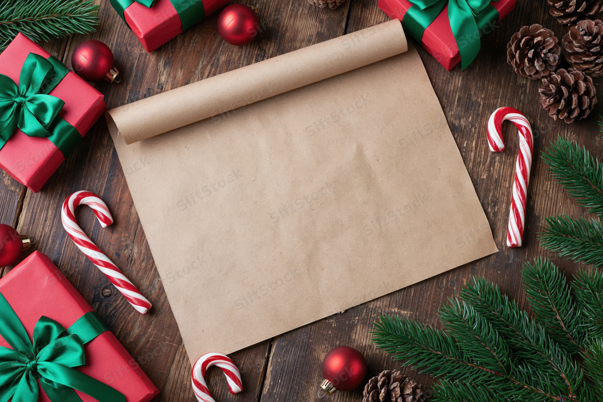 Blank parchment scroll on wooden table surrounded by christmas gifts and decorations