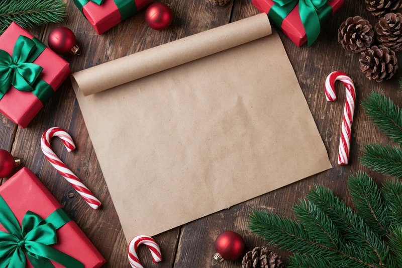 Blank parchment scroll on wooden table surrounded by christmas gifts and decorations