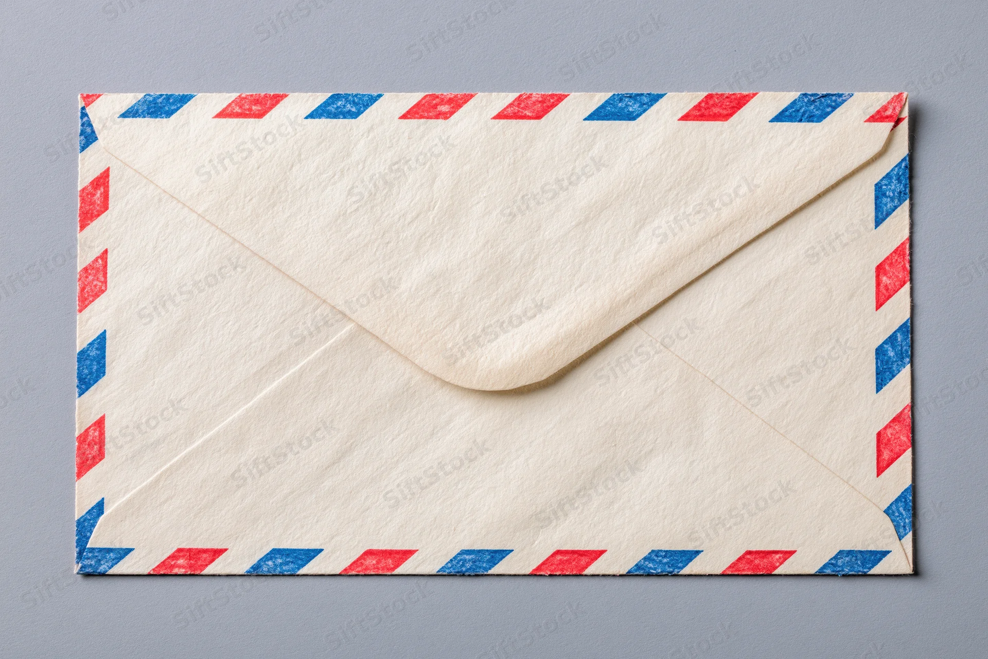 Closed airmail envelope with red and blue striped pattern lying flat on gray surface