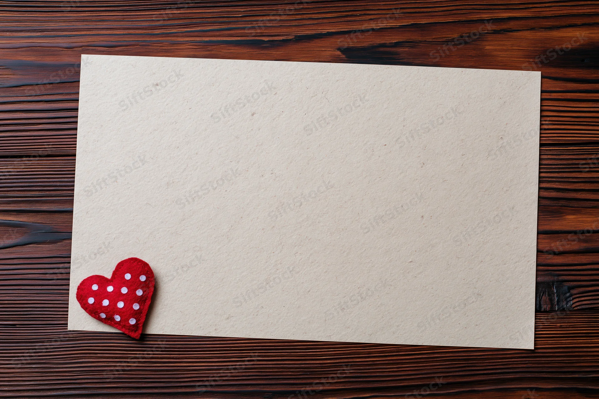 Blank cream paper sheet with red polka dot felt heart on dark wooden table
