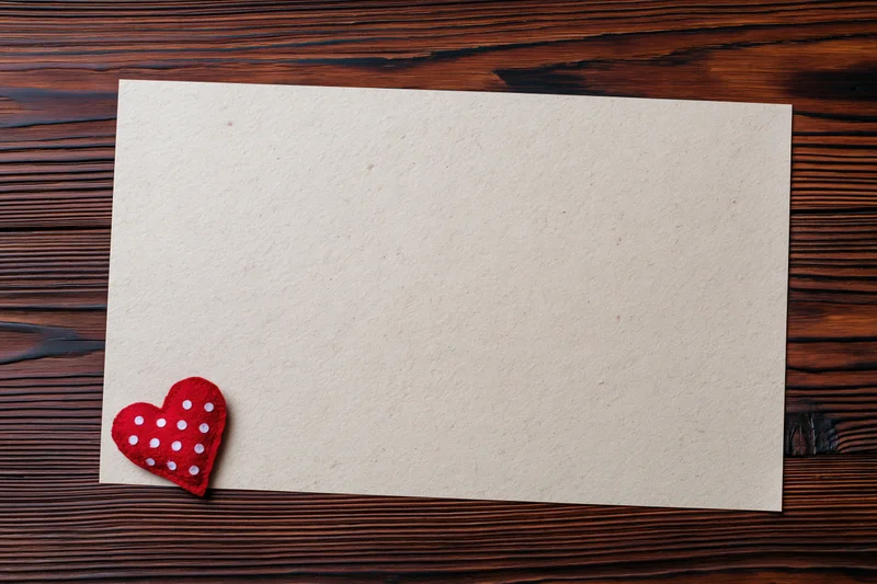 Blank cream paper sheet with red polka dot felt heart on dark wooden table