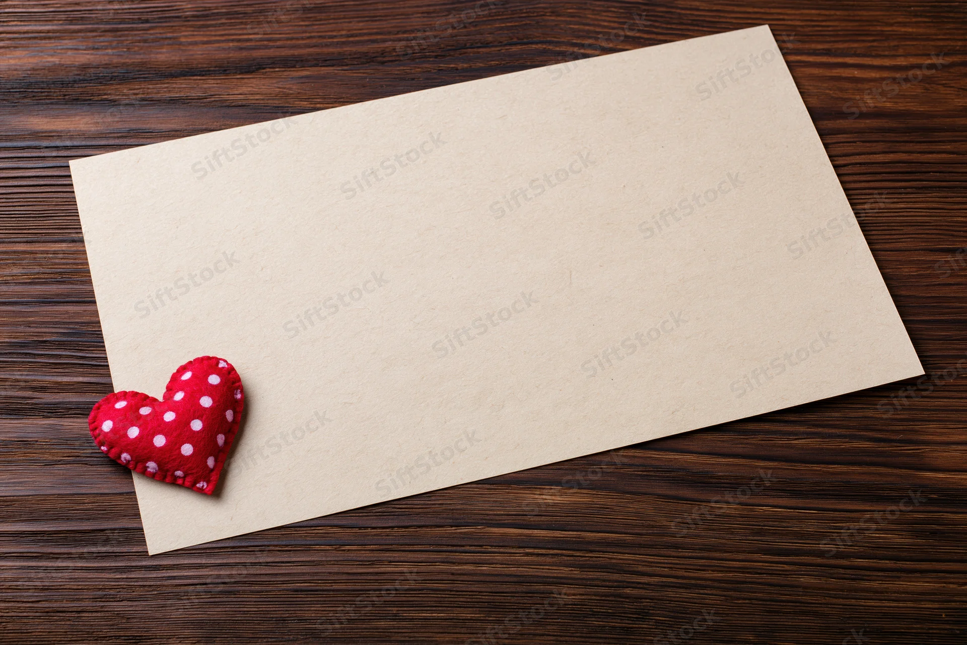 Blank craft paper sheet with red polka dot felt heart on dark wooden surface