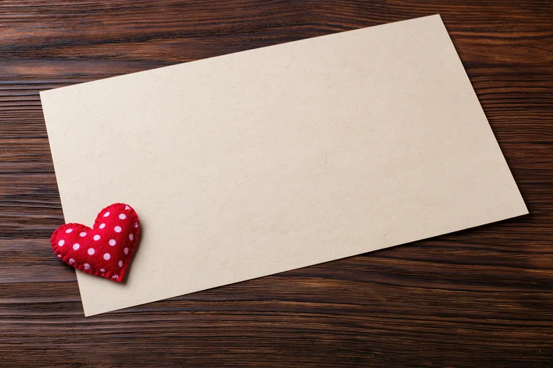 Blank craft paper sheet with red polka dot felt heart on dark wooden surface