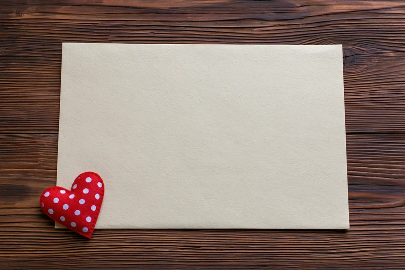 Blank cream paper sheet with red polka dot heart on dark wooden surface