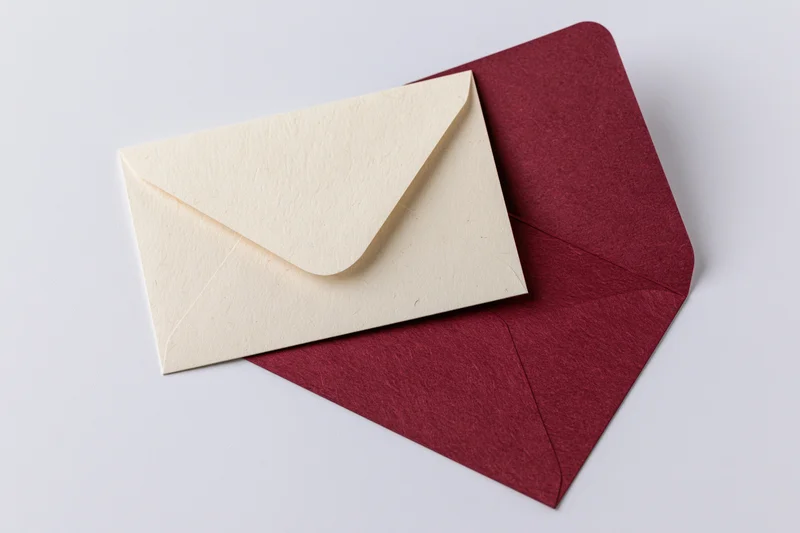 Two envelopes, one cream and one red, arranged on a white surface with copyspace